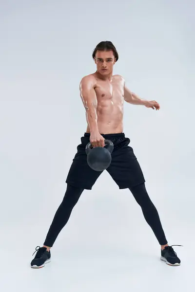 Handsome athletic shirtless man exercising with kettlebell and looking at camera on gray backdrop — Stock Photo