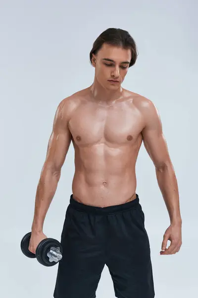 Appealing young shirtless man in black comfy pants exercising with dumbbell and looking away — Stock Photo