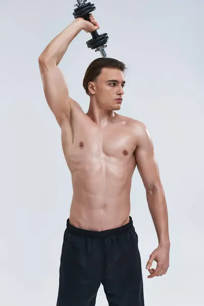 Attraente giovane uomo senza maglietta in pantaloni neri comodi esercizio con manubri e distogliendo lo sguardo — Foto stock