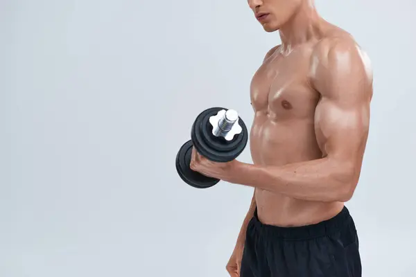 Cropped view of young muscular man in black pants exercising with dumbbell on gray background — Stock Photo