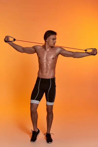 Atractivo joven deportista hombre en pantalones cortos negros posando en topless y haciendo ejercicio con expansor de fitness - foto de stock