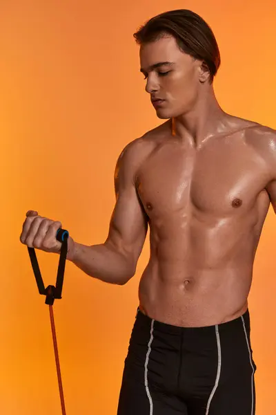 Atractivo joven deportista en pantalones cortos negros posando en topless y haciendo ejercicio con expansor de fitness - foto de stock