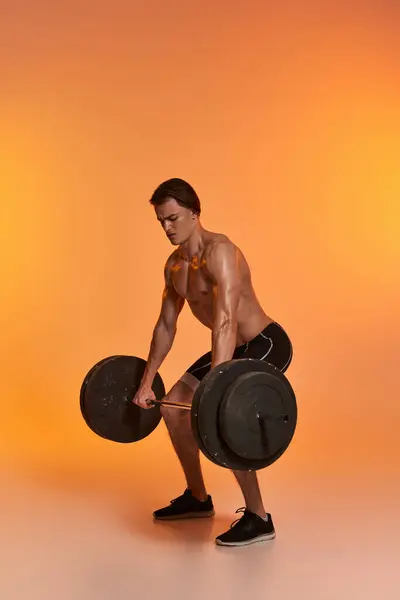 Appealing shirtless muscular man in black pants exercising with barbell on vibrant orange backdrop — Stock Photo