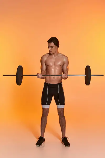 Atractivo hombre musculoso sin camisa en pantalones negros ejercicio con barra de pesas en vibrante fondo naranja - foto de stock