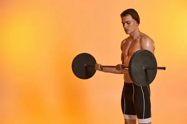 Handsome shirtless muscular man in black pants exercising with barbell on vibrant orange backdrop — Stock Photo