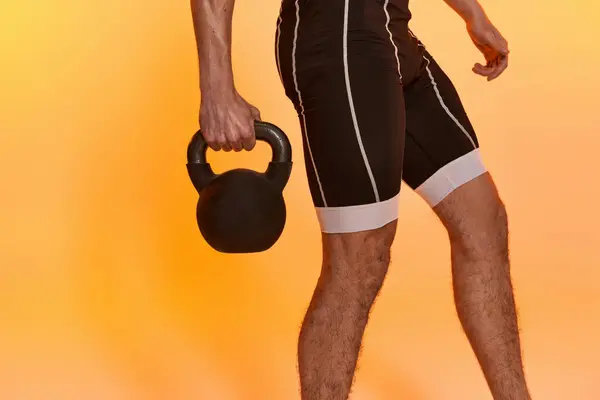 Cropped view of young athletic man posing topless and exercising with kettlebell on orange backdrop — Stock Photo