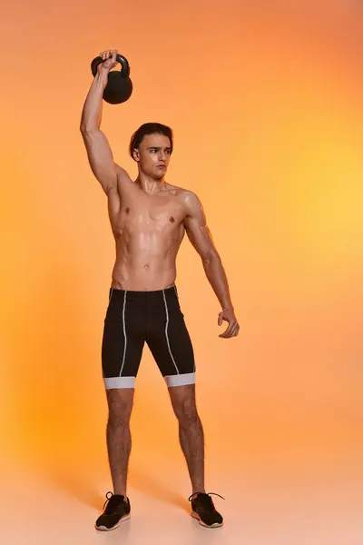 Hombre atlético sin camisa de buen aspecto haciendo ejercicio activamente con kettlebell sobre fondo vivo naranja - foto de stock