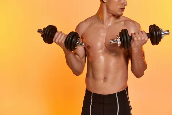 Cropped view of sexy muscular man posing topless while training with dumbbells on orange backdrop — Stock Photo