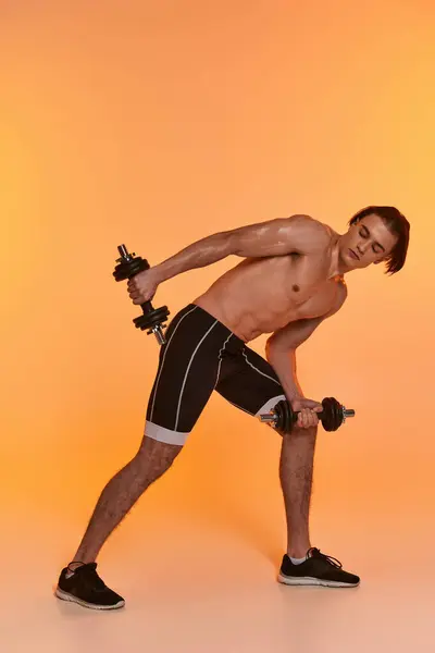Good looking muscular shirtless man in black sport shorts training with dumbbells on vivid backdrop — Stock Photo