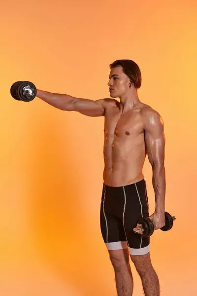 Attractive muscular shirtless man in black sport shorts training with dumbbells on vivid backdrop — Stock Photo