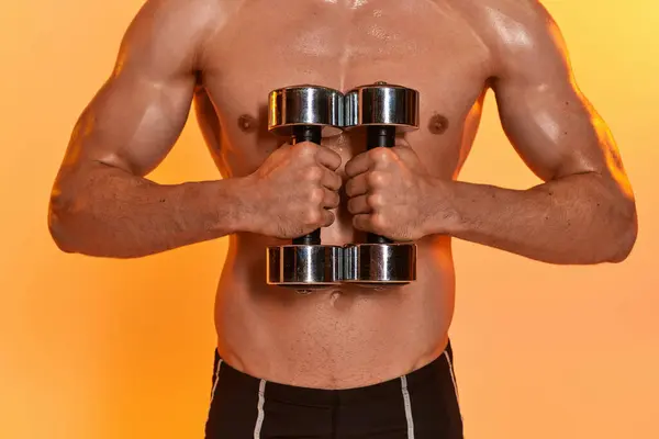Cropped view of sexy muscular man posing topless while training with dumbbells on orange backdrop — Stock Photo