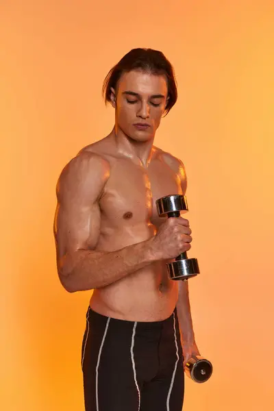 Appealing muscular shirtless man in black sport shorts training with dumbbells on vivid backdrop — Stock Photo