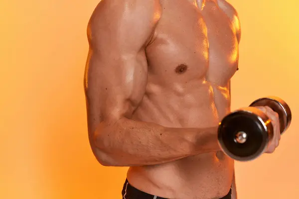 Cropped view of sexy muscular man posing topless while training with dumbbell on orange backdrop — Stock Photo