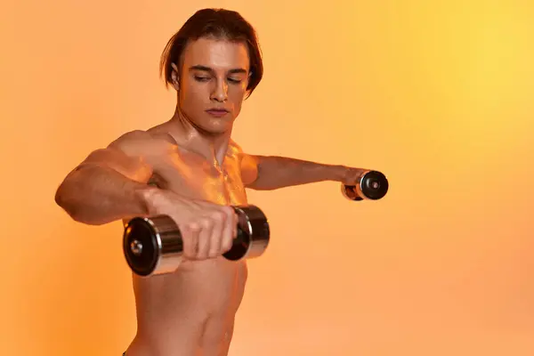 Handsome muscular shirtless man training with dumbbells on vibrant orange backdrop and looking away — Stock Photo