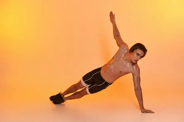 Good looking shirtless man in black shorts exercising actively and looking away on orange backdrop — Stock Photo