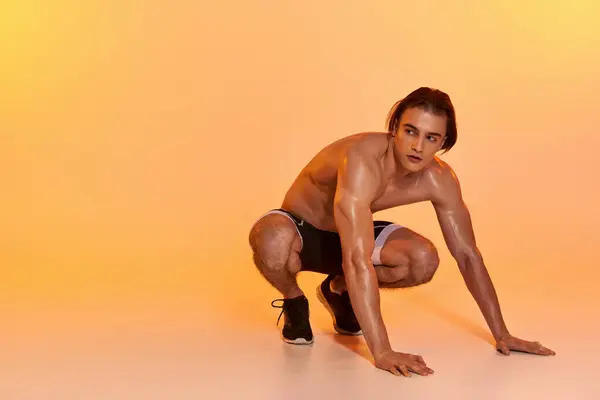 Attraente uomo senza maglietta in pantaloncini neri esercizio attivo e guardando lontano su sfondo arancione — Foto stock