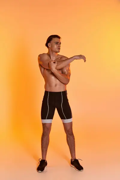 Handsome shirtless man in black shorts exercising actively and looking away on orange backdrop — Stock Photo