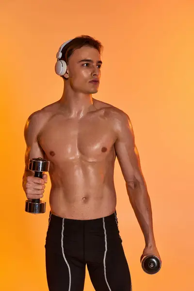 Atractivo hombre musculoso en pantalones cortos negros con auriculares haciendo ejercicio con mancuernas y mirando hacia otro lado - foto de stock