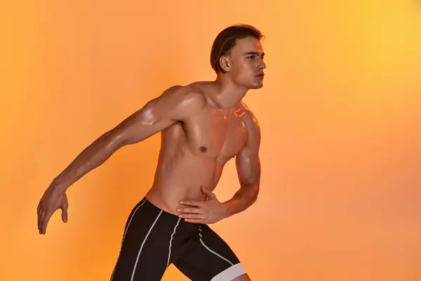 Gut aussehender junger athletischer Mann posiert oben ohne in aktiven Bewegungen auf orangefarbenem Hintergrund — Stockfoto