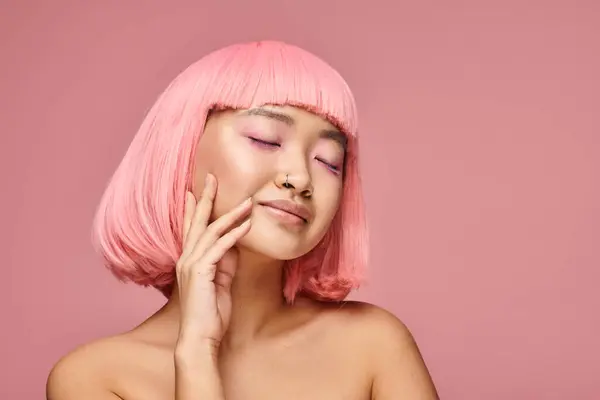Азиатская женщина с розовыми волосами и закрытыми глазами, касающимися ее щеки на ярком фоне — стоковое фото