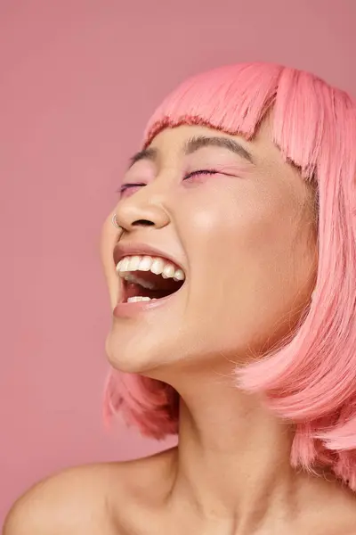 Asiatique femme dans son 20s avec rose cheveux et maquillage rire sur vibrant fond — Photo de stock