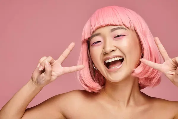 Attrayant asiatique femme avec nez percing montrant signe de paix et sourire sur fond vibrant — Photo de stock