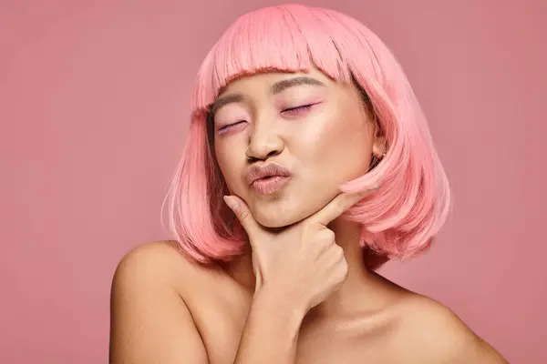 Alluring asian woman in 20s with pink hair and makeup kissing with hand on vibrant background — Stock Photo