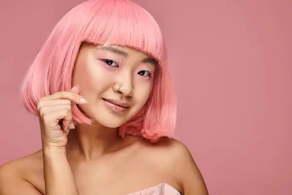 Encantadora mujer joven asiática con piercing en la nariz mostrando el signo del corazón y sonriendo en un fondo vibrante - foto de stock