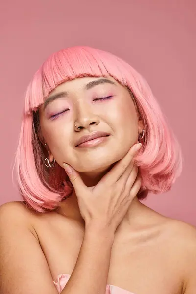 Seductora mujer con el pelo rosa tocando su barbilla con la mano con los ojos cerrados sobre un fondo vibrante - foto de stock