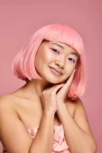 Hermosa mujer asiática con pelo rosa y maquillaje sonriendo con las manos contra el fondo vibrante - foto de stock