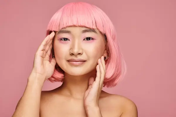 Encantadora mujer asiática de 20 años con piercing en la nariz posando con las manos sobre un fondo vibrante - foto de stock