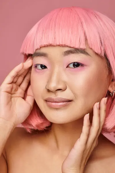 Hermosa asiático joven mujer con rosa maquillaje posando con manos sobre vibrante fondo - foto de stock