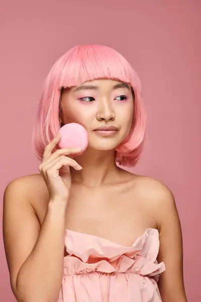 Linda asiático jovem menina com rosa cabelo olhando para o lado e segurando para macaroon no vibrante fundo — Fotografia de Stock