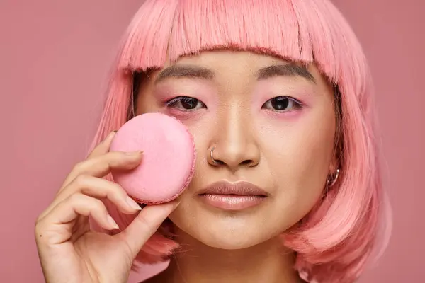 Close up attractive asian woman with pink hair posing with macaroon on vibrant background — Stock Photo