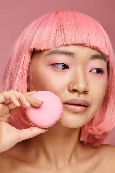 Vicino asiatico donna con rosa capelli posa con macaroon e cercando per lato su vibrante sfondo — Foto stock