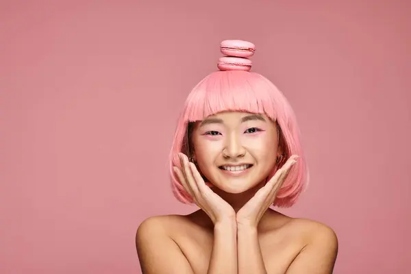 Счастливая азиатская молодая женщина с розовыми волосами, руками и макаронами на голове на ярком фоне — стоковое фото