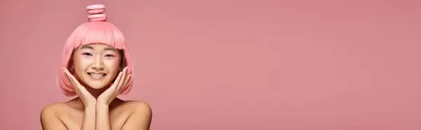 Банер милої азіатки з рожевим волоссям, руками і макарунами на голові на яскравому фоні — стокове фото