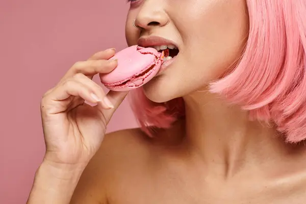 Cropped shot of young woman with pink hair eating macaroon against vibrant background — Stock Photo