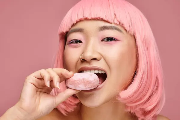 Portrait of happy asian young woman with pink hair eating mochi against vibrant background — Stock Photo