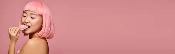 Striscione di asiatico ragazza in suo 20s con rosa capelli mangiare mochi oltre spalla contro vibrante sfondo — Foto stock