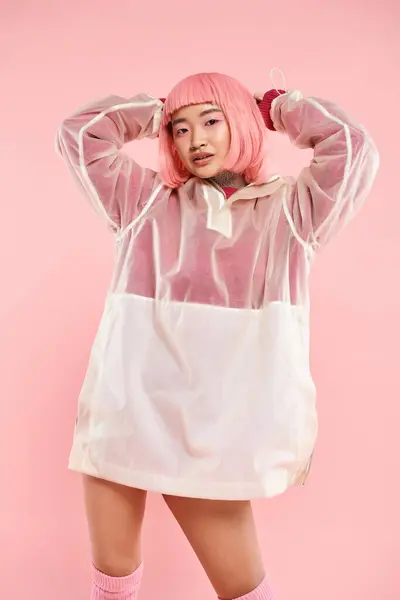 Elegante sorrindo asiático mulher no 20s com rosa cabelo posando com as mãos na cabeça no vibrante fundo — Fotografia de Stock