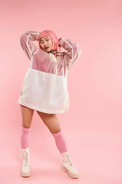 Encantador asiático joven mujer con rosa pelo y maquillaje posando con las manos en la cabeza en vibrante fondo - foto de stock