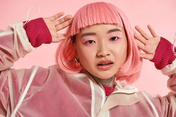 Atractivo asiático joven mujer con rosa pelo y maquillaje posando con las manos en vibrante fondo - foto de stock