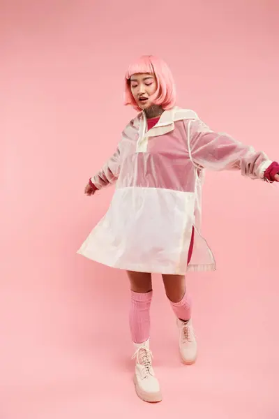 Веселая азиатская молодая девушка с розовыми волосами в стильном наряде крутится на ярком фоне — стоковое фото