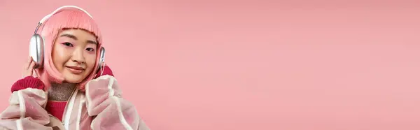 Tiro horizontal de mujer asiática con pelo rosa posando con auriculares sobre fondo vibrante - foto de stock