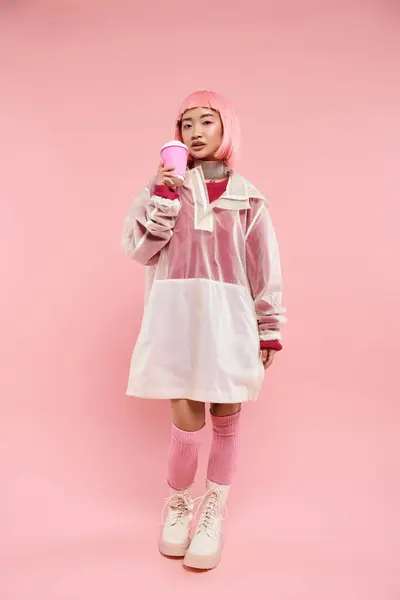 Заманчивая азиатская молодая девушка с розовыми волосами пьет с чашкой кофе на ярком фоне — стоковое фото