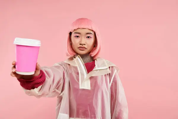 Hermosa mujer asiática con pelo rosa sosteniendo la taza de café contra el fondo vibrante - foto de stock