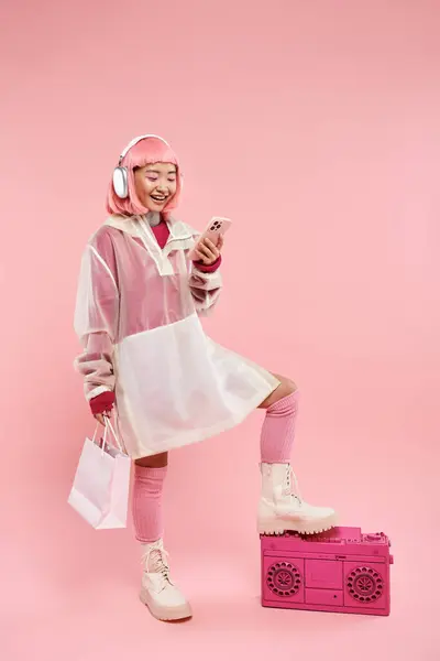 Linda mulher asiática em fones de ouvido mensagens no smartphone e segurando com pacotes de compras — Fotografia de Stock