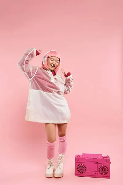 Joyeuse jeune femme avec les cheveux roses dans les écouteurs dansant avec de la musique sur fond vibrant — Photo de stock