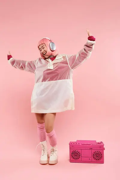 Feliz asiático jovem mulher com cabelo rosa em fones de ouvido dançando com música em fundo vibrante — Fotografia de Stock